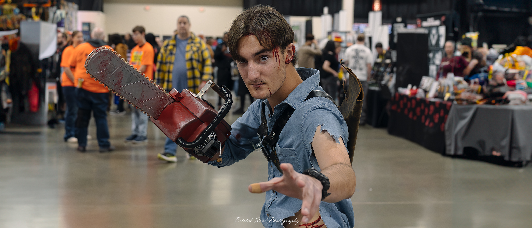 A cosplayer dressed as Ash Williams from *Evil Dead*, featuring a rugged outfit, iconic chainsaw hand, and determined expression, standing in a dynamic pose that captures the essence of the character's battle-hardened personality.